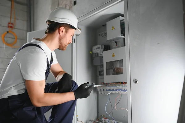 A male electrician works in a switchboard with an electrical connecting cable