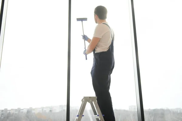 An employee of a professional cleaning service washes the glass of the windows of the building. Showcase cleaning for shops and businesses