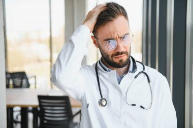 Stresli erkek doktor. Yetişkin bir erkek doktor uzun saatler çalışıyor. Ofisinde çok çalışan bir doktor. Doktorlar bile tükenmekten muaf değildir..