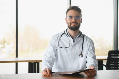 Doktor adam çalıştığı yerdeki masada oturuyordu. Klinikte mükemmel bir tıbbi hizmet. Yakışıklı genç bir doktorun portresi.