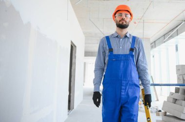 Tamamlanmamış büyük bir odada poz veren genç ve çalışkan bir inşaatçının portresi. İnşa kavramı.