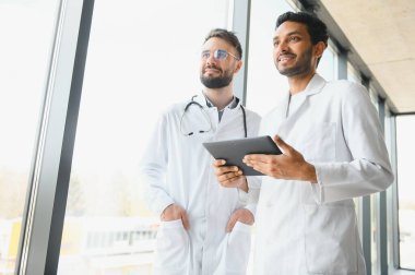 An Indian doctor and a European doctor stand together in a hospital lobby.