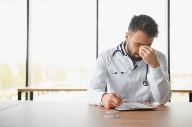 Üzgün sağlık görevlisinin ellerle kafasını kapattığı yakın plan. Ofiste oturan depresif erkek doktor. Steteskop insanların boynunda. Modern tıp ve sağlık konsepti