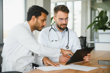 An Indian doctor and a European doctor stand together in a hospital lobby.