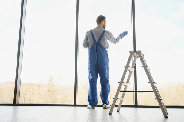 stock image Male janitor cleaning window in office.