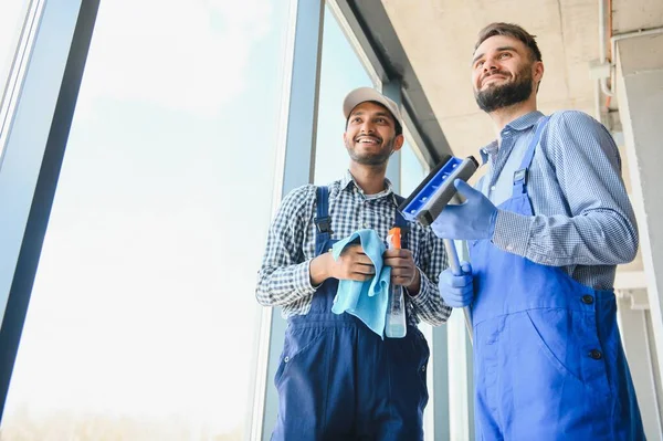 stock image multiethnic professional cleaners in uniform washing large windows in office.