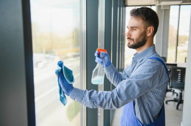 Erkek profesyonel temizlik işçisi özel ekipmanlı bir mağazanın camlarını ve pencerelerini temizliyor..