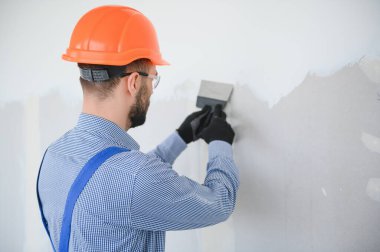 Alçıpan işçisi ya da zımpara kağıdı tutacağı kullanarak sıva tahtası duvarlarını sıva ile zımparalıyor. Beyaz baret ve güvenlik gözlüğü takıyordu. Kopyalama alanı olan panoramik resim.