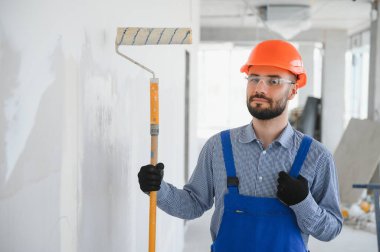 Tamamlanmamış büyük bir odada poz veren genç ve çalışkan bir inşaatçının portresi. İnşa kavramı.