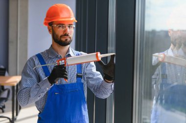 Evdeki oturma odasına plastik pencereler monte eden ya da ayarlayan işçi.