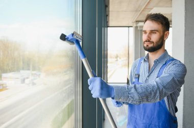 Erkek profesyonel temizlik işçisi özel ekipmanlı bir mağazanın camlarını ve pencerelerini temizliyor..