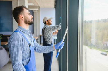 Sakallı adam ofis pencerelerini yıkıyor. Çok kültürlü kadınların yanında, pankartta..