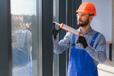 Workers with tube of sealant and suction lifters installing plastic windows indoors