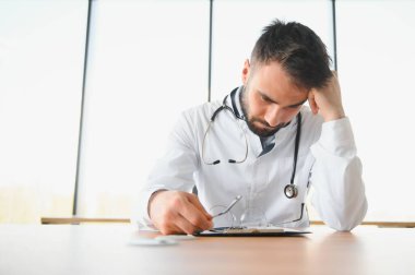 Doktor adam çalıştığı yerdeki masada oturuyordu. Klinikte mükemmel bir tıbbi hizmet. Yakışıklı genç bir doktorun portresi.