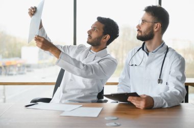 An Indian doctor and a European doctor stand together in a hospital lobby.