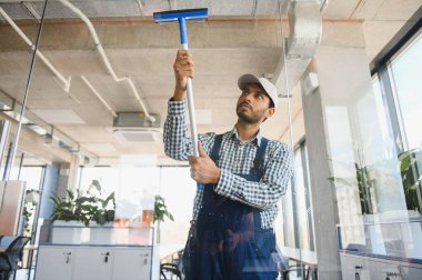 Ofisin camlarını silen genç Hintli adam..