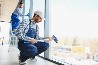 Üniformalı çok ırklı profesyonel temizlikçiler ofiste büyük camları yıkıyorlar..