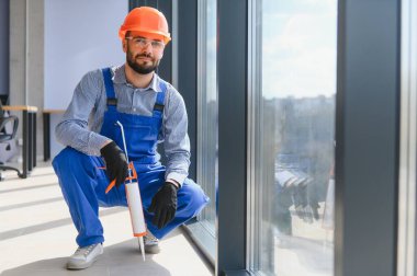 Workers with tube of sealant and suction lifters installing plastic windows indoors