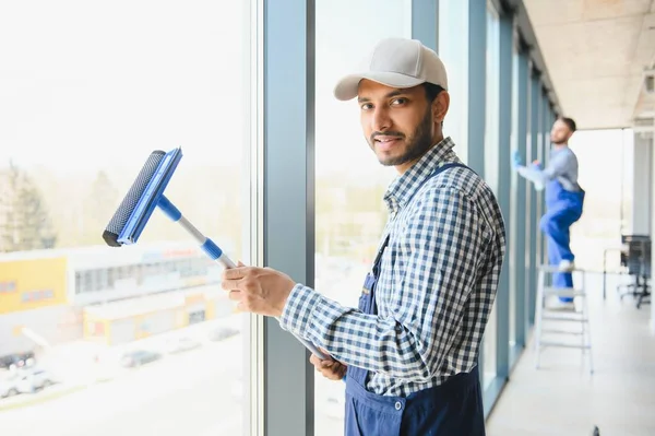 stock image Young indian man washing window in office