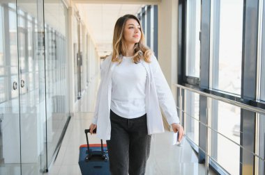 Uluslararası havaalanında bavulları olan şık, genç bir bayan. Vergisiz alışveriş bölgesinde uçağını bekliyor.