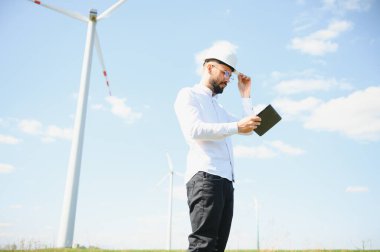 Mühendis rüzgar türbinindeki enerji üretimini kontrol ediyor. Yel değirmenleri parkında çalışan bir işçi.