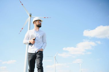 Mühendis rüzgar türbinindeki enerji üretimini kontrol ediyor. Yel değirmenleri parkında çalışan bir işçi.