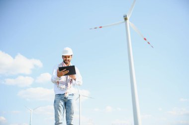 Yel değirmeni çiftliğinde çalışan Hintli mühendis elektrik üretiyor. Alternatif yeşil enerjili rüzgar türbini tarım jeneratörü. Asyalı mühendis elektrik gücünü kontrol ediyor.