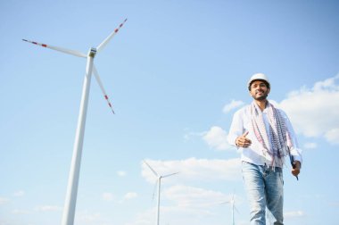 Rüzgâr türbinleriyle tarlada duran odaklanmış Hintli adamın portresi..