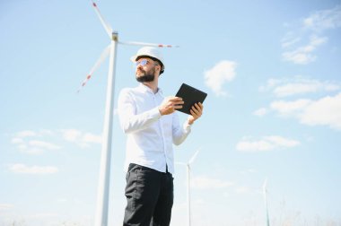Mühendis rüzgar türbinindeki enerji üretimini kontrol ediyor. Yel değirmenleri parkında çalışan bir işçi.