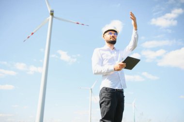 Mühendis rüzgar türbinindeki enerji üretimini kontrol ediyor. Yel değirmenleri parkında çalışan bir işçi.