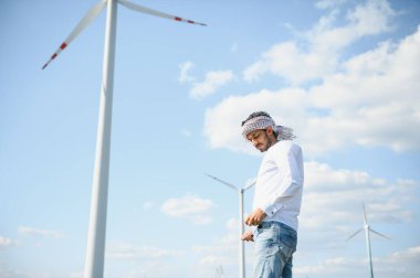 Rüzgâr türbinleriyle tarlada duran odaklanmış Hintli adamın portresi..