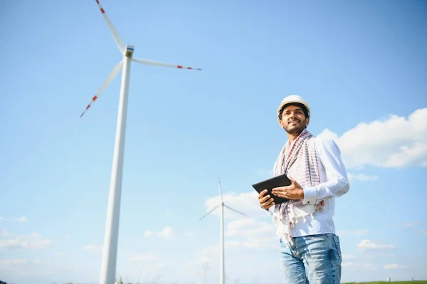 stock image Engineer India man working at windmill farm Generating electricity clean energy. Wind turbine farm generator by alternative green energy. Asian engineer checking control electric power.