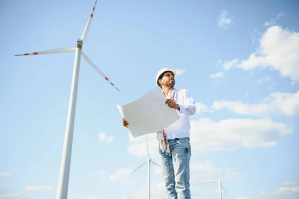 stock image Engineer India man working at windmill farm Generating electricity clean energy. Wind turbine farm generator by alternative green energy. Asian engineer checking control electric power.