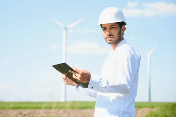 Indian Engineer in wheat field checking on turbine production.