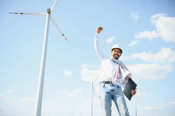 Engineer India man working at windmill farm Generating electricity clean energy. Wind turbine farm generator by alternative green energy. Asian engineer checking control electric power.