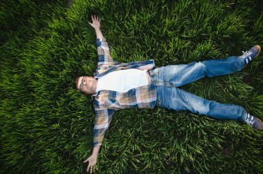 Yeşil buğday tarlasında yatan mutlu çiftçi. Agronomist doğada dinleniyor.