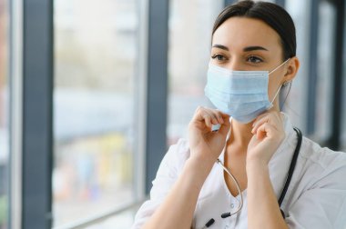 Üniforma ve koruyucu maske takan genç, güzel bir kadın doktor portresi..