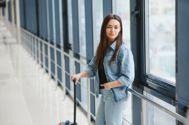 Havaalanı terminalinde bavulu çeken genç bir kadın. Boşluğu kopyala.