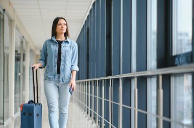 Havaalanı terminalinde bavulu çeken genç bir kadın. Boşluğu kopyala.