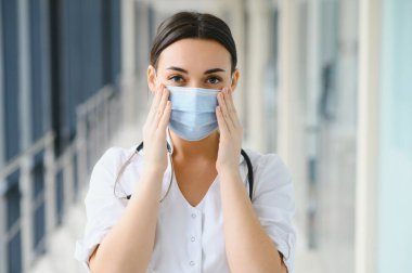 Üniforma ve koruyucu maske takan genç, güzel bir kadın doktor portresi..
