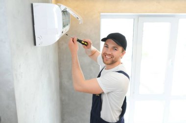 Müşteri evinde gülümseyen genç erkek elektrikçi tamircisi. Tamirci ya da tamirci, müşteri evindeki havalandırma cihazındaki filtreleri tamir eder..
