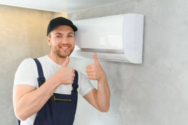 Müşteri evinde gülümseyen genç erkek elektrikçi tamircisi. Tamirci ya da tamirci, müşteri evindeki havalandırma cihazındaki filtreleri tamir eder..