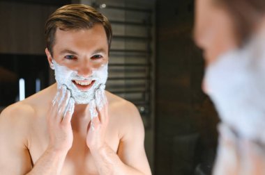 Yarısı bitti. Yakışıklı, genç, üstsüz adam yüzüne tıraş olmak için başvuruyor.