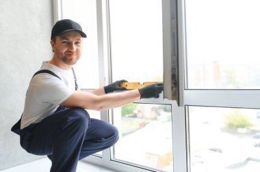 Yakışıklı genç adam yeni ev şantiyesine pencere takıyor..