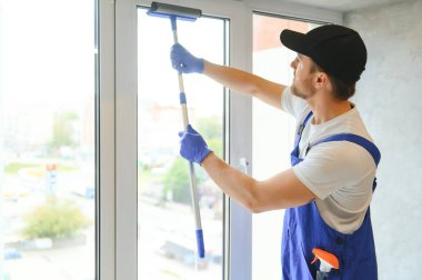 Erkek profesyonel temizlik işçisi tulumlu pencereleri temizliyor.