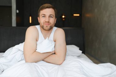 Genç adam uyanıyor ve elleri kalkıyor. Sabahları beyaz yatakta uzanıyor. Pencereden güneş ışığı geçiyor..