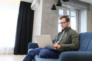 Kanepede dizüstü bilgisayarla oturan neşeli genç adam..