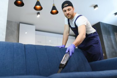 Temizlikçi elinde modern çamaşır süpürgesi ve kirli kanepeyi profesyonel deterjanla lekeyle temizliyor. Ev kavramında profesyonel bahar temizliği.