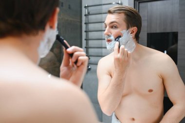 Olgun yakışıklı adam aynanın önünde tıraş oluyor..