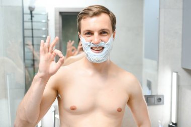 Yakışıklı delikanlı yüzünü tıraş ve aynaya bakıyor